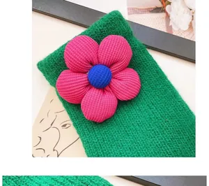 Close-up of green winter knit gloves featuring a cute 3D pink flower and blue center design.