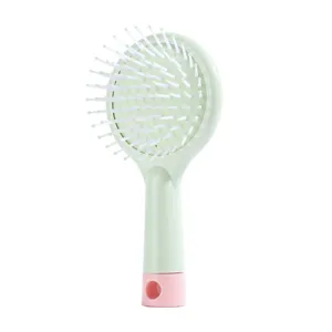 Mini air cushion hairbrush detail view, cute pink and green plastic handle with bristle close up.