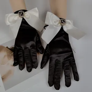 Primo piano di eleganti guanti in raso nero con grandi fiocchi bianchi e dettagli in strass.