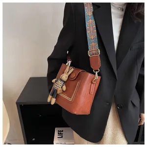 Detail shot of a vintage brown leather shoulder bag with wide strap and cute rabbit pendant.