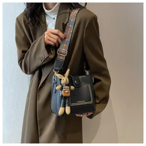 Detailed close-up of trendy black leather shoulder bag featuring colorful strap and bunny charm.