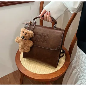 Close-up detail view of retro brown leather backpack with cute plush bear charm and embossed text.
