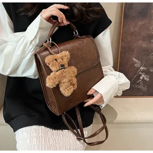 Detailed view of vintage brown leather backpack featuring cute plush bear pendant and flap design.