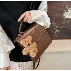 Detailed view of vintage brown leather backpack featuring cute plush teddy bear charm pendant.