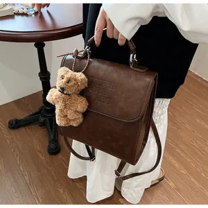 Vintage brown leather backpack detail view showing cute plush bear pendant and letters.
