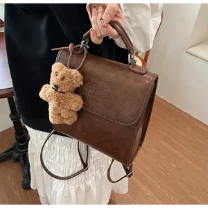 Vintage brown casual leather backpack with cute teddy bear charm detail for students daily use.