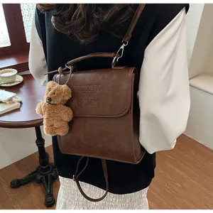 Retro fashion casual brown PU leather backpack detail view with cute bear pendant and debossed letters.