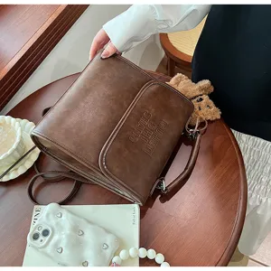 Vintage brown leather backpack detail view with embossed lettering and cute teddy bear pendant.