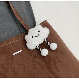 Detailed view of the brown tote bag featuring a cute fluffy cloud charm with dangling pom-poms.