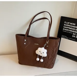 Detail view of retro brown tote bag with cute plush cloud charm, stylish underarm shoulder bag.