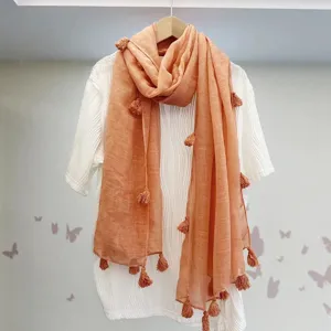 Detailansicht eines orangefarbenen Quasten-Baumwoll-Leinenschals für Damen an weißem Shirt.