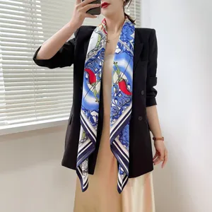 Nahaufnahme des eleganten blauen Seidenschals mit roten Chilimotiven und klassischen Streifenrändern.