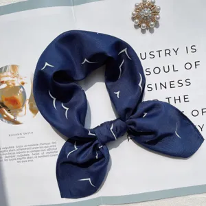 Close-up detail of dark blue silk square scarf with white bird print and pearl brooch prop.