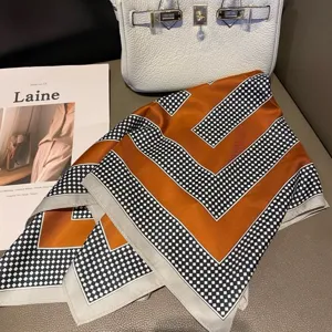 Primer plano detallado de un pañuelo cuadrado con estampado geométrico en naranja, negro y blanco.