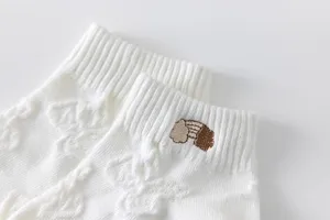 Close-up detail of women's white short socks featuring cute embroidered rainbow and cloud pattern.