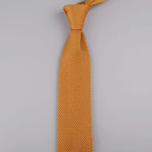 Primo piano di una cravatta in maglia giallo senape, con trama fine e dettaglio a punta.