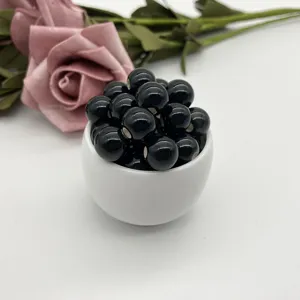 Detailed view of glossy black ceramic loose beads placed in a white cup, ideal for DIY jewelry crafting.