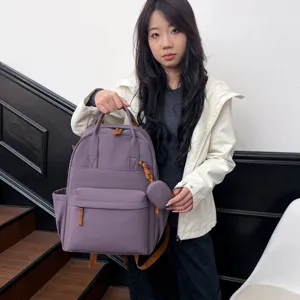 Detailansicht des lila Studentenrucksacks mit braunen Akzenten, Fronttasche und kleiner Hängeltasche.