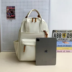 Detailansicht des großen cremeweißen Canvas-Schulrucksacks mit mehreren Taschen und Riemen.