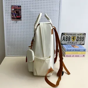 Detailansicht des weißen Canvas-Schulrucksacks mit braunen Trägern und kleinen Taschen.