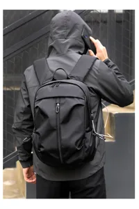Detail view of a black minimalist men's USB charging backpack worn by model outdoors.