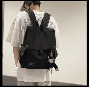 Detail shot of the casual black backpack featuring a flap, multiple pockets, and monkey keychain.