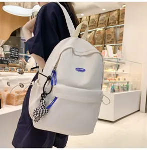 Detailansicht des weißen minimalistischen Rucksacks mit blauem Logo und modischem Anhänger.