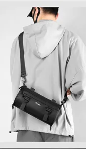 Men's black laminated cylindrical crossbody chest bag with adjustable strap and zip detail.
