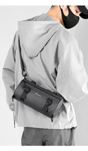 Detail shot of stylish black cylindrical messenger bag worn by male model with adjustable strap.