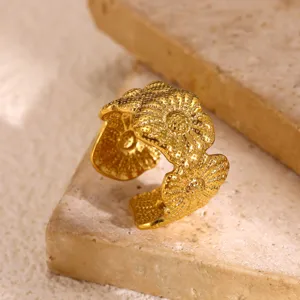 Gedetailleerde opname van een vergulde brede open ring met gestructureerd bloemenpatroon.