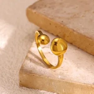 Close-up detail van minimalistische vergulde roestvrijstalen open ring met moderne bolletjes.