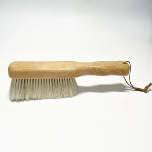 Vue détaillée de la brosse de nettoyage en bois avec poils blancs souples et une lanière en cuir.