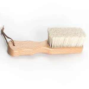 Brosse à chaussures en bois avec poils souples blancs et lanière en cuir pour le nettoyage.