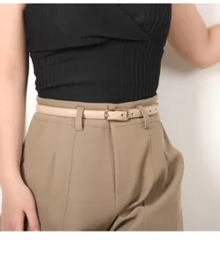Detailed view of women thin leather belt with golden buckle styling on casual trousers.