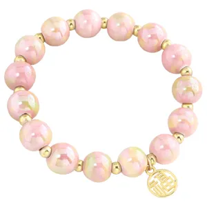 Bracelet en perles de céramique rose avec perles d'espacement dorées et charm porte-bonheur.