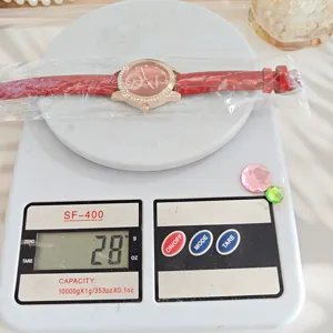 Detailansicht einer Damenuhr mit rotem Lederarmband und Strasssteinen auf der Waage.