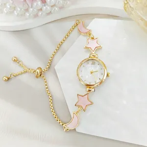 Detail view of women watch featuring pink star and moon charms on gold pull chain bracelet.
