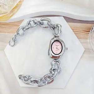 Gros plan montre femme chaîne métal irrégulière, cadran rose avec strass, bracelet.