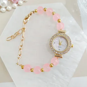 Detailed closeup of women pink beaded quartz watch with sparkly rhinestone dial and gold chain.