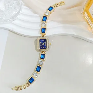 Elegante reloj de mujer con gemas azules rectangulares y cristales en pulsera dorada.