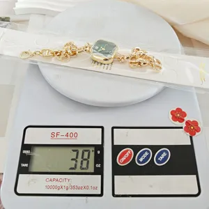 Detailaufnahme quadratische Damenuhr mit grünem Zifferblatt und goldener Kette beim Wiegen.