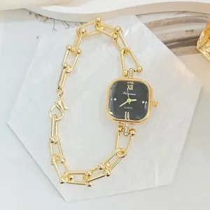 Nahaufnahme einer luxuriösen quadratischen Quarzuhr mit schwarzem Zifferblatt und Goldkette.