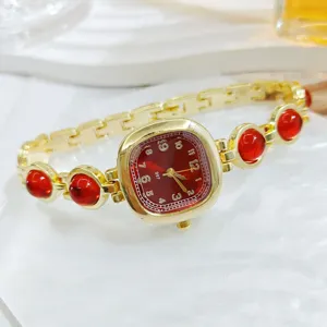 Vista detallada de un reloj de mujer dorado de lujo con pulsera de piedras rojas y esfera.