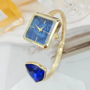 Eckige Quarz Armreif Uhr Detail, elegantes goldenes Metallarmband mit blauem Stein für Damen.