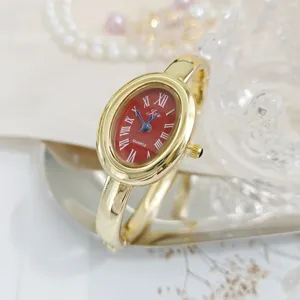 Gold-tone oval quartz bangle watch with striking red Roman numeral dial for women.