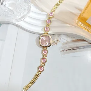 Vista detallada de reloj de pulsera dorado para mujer con elegante esfera rosa y gemas brillantes.