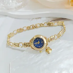 Goldfarbene Quarz-Armbanduhr Detailaufnahme mit blauem Zifferblatt und Herz-Anhänger.