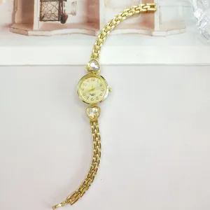 Gold tone quartz women watch detail showing heart crystal pendant and delicate link strap.