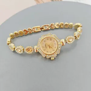 Detalle de un reloj de cuarzo dorado para mujer con bisel floral de estrás y pulsera de cristal.