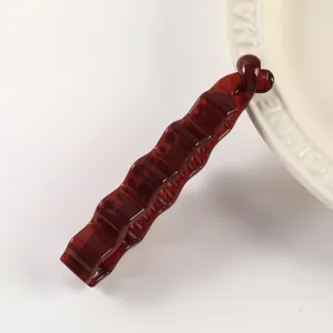 Dark red plastic banana hair clip closeup, irregular wavy design, minimalist ponytail accessory.